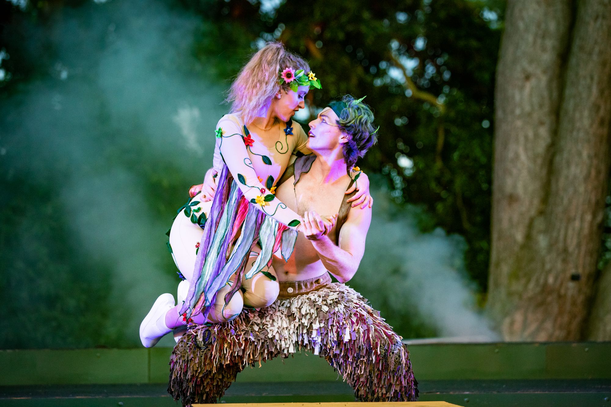 Two performers embracing in colourful woodland costumes
